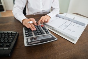 Close-up Of Businessperson Calculating Financial Expenses With Calculator At Desk